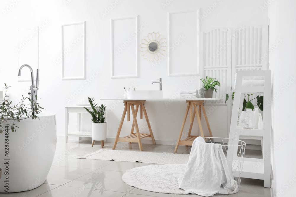 Interior of light bathroom with white sink, bathtub and houseplants