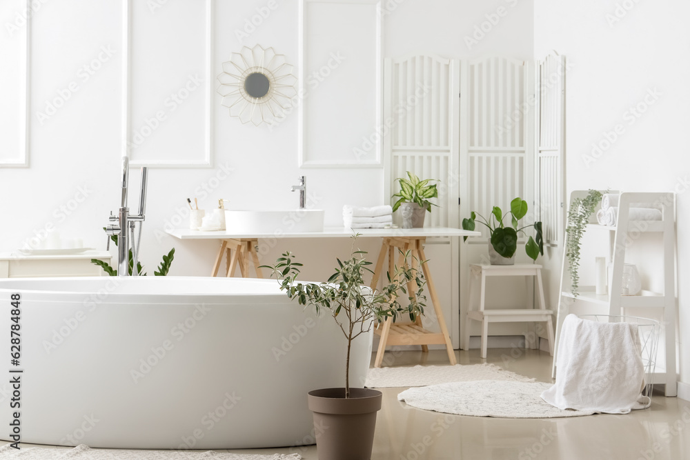 Interior of light bathroom with white sink, bathtub and houseplants