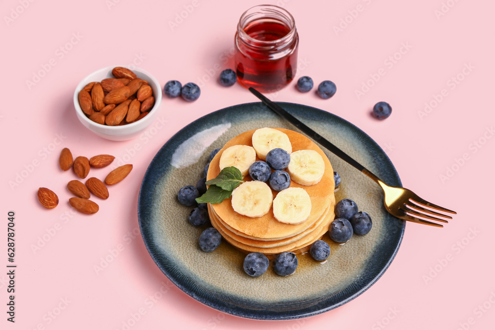 Plate with sweet pancakes, nuts and honey on pink background