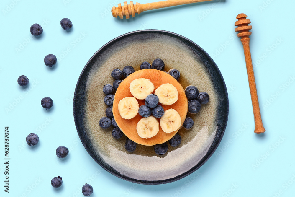 Plate with sweet pancakes, banana and blueberry on blue background