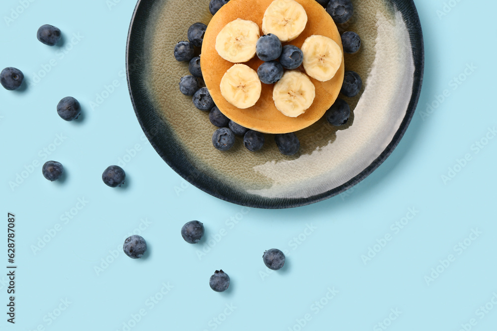 Plate with sweet pancakes, banana and blueberry on blue background