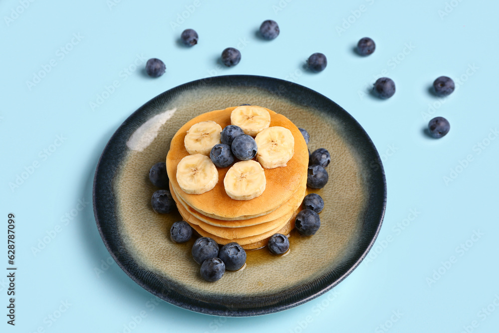 Plate with sweet pancakes, banana and blueberry on blue background