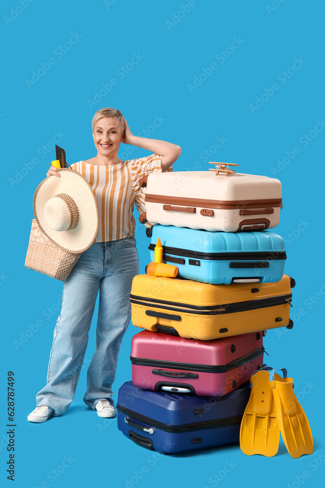 Mature woman with suitcases on blue background