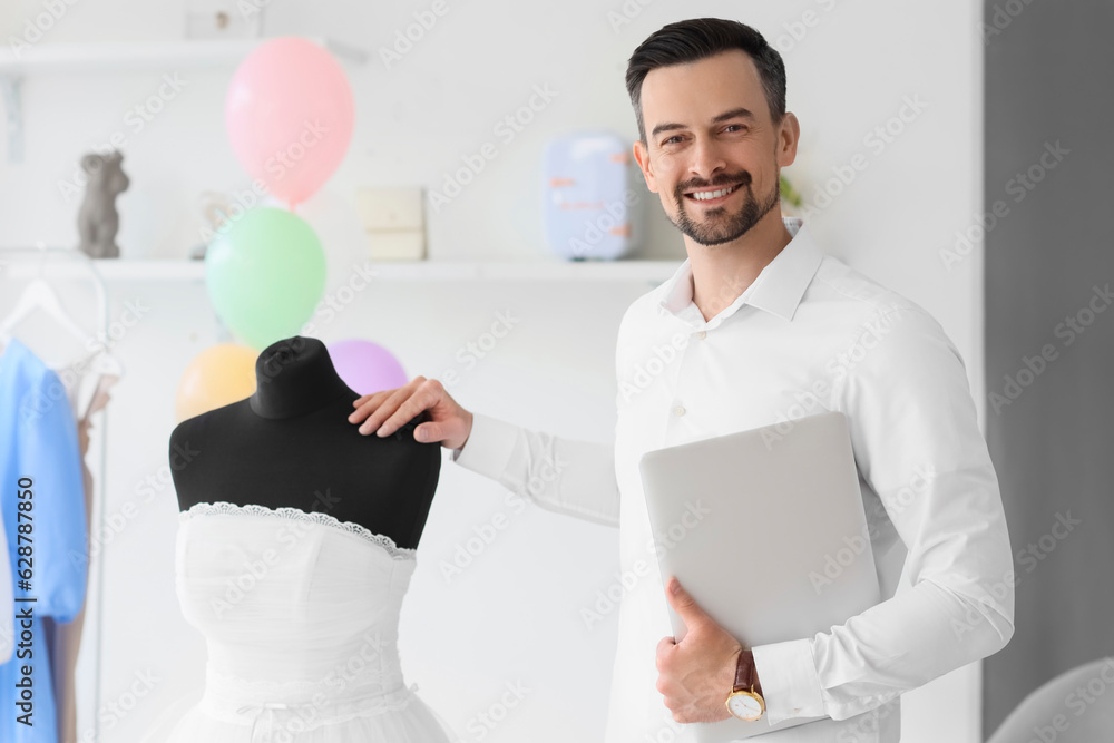 Male wedding planner with laptop and dress in office