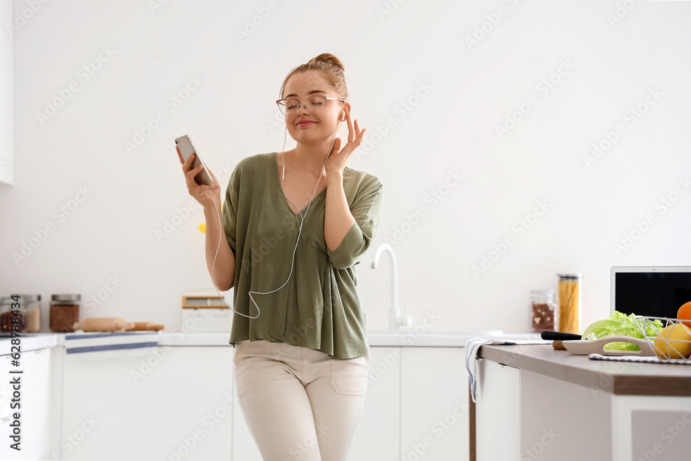 Pretty young woman listening to music and dancing in light kitchen