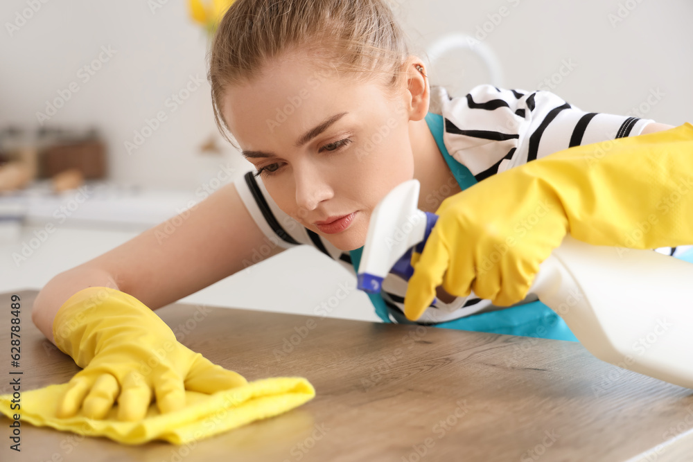 Pretty young woman in yellow rubber gloves cleaning dining table with rag and detergent