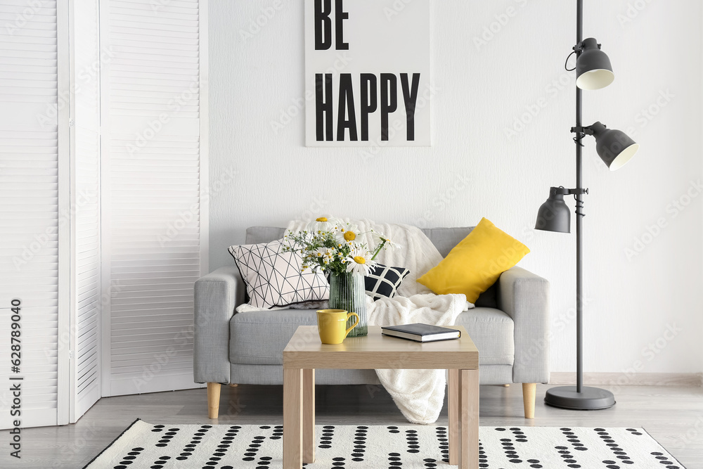 Interior of stylish living room and vase with blooming chamomile flowers on wooden table