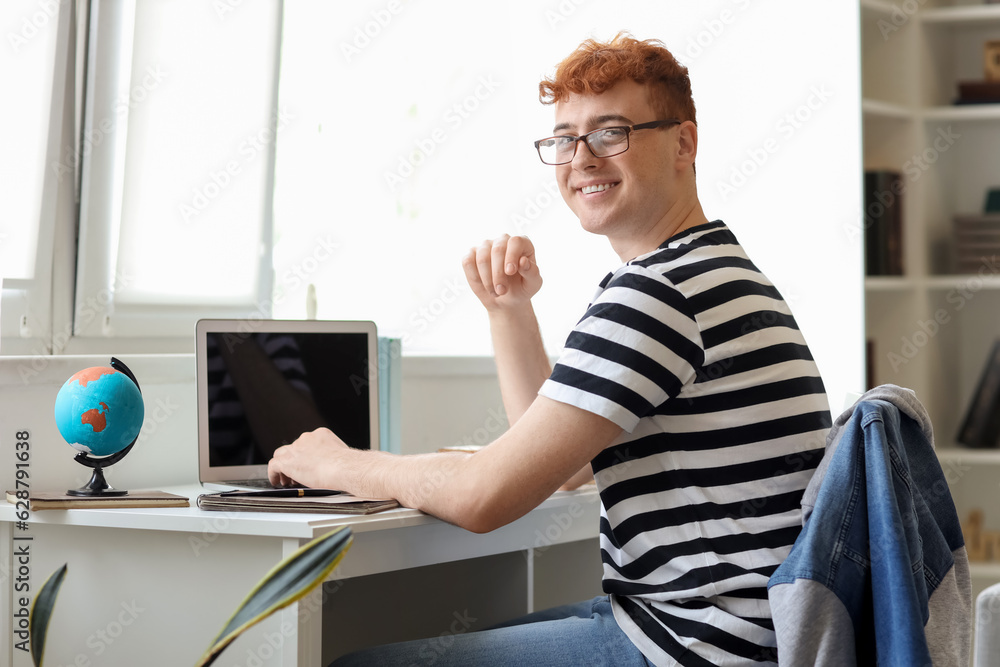 Young redhead man studying with laptop at home