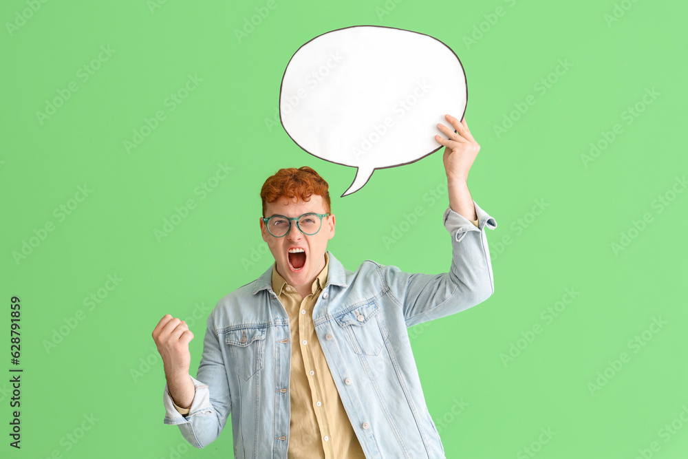 Angry young redhead man with blank speech bubble on green background