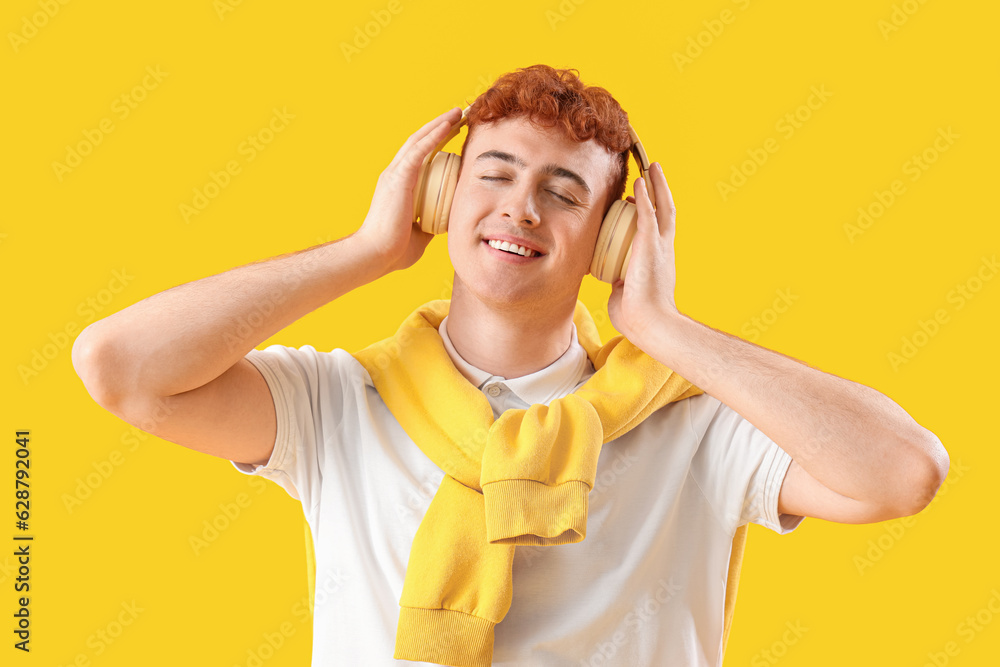 Young redhead man in headphones listening to music on yellow background