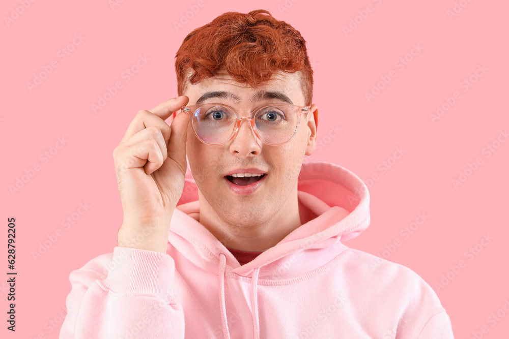 Surprised young redhead man in eyeglasses on pink background, closeup