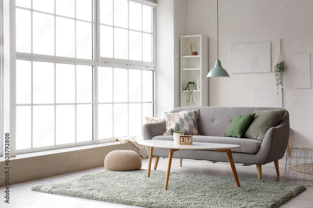 Interior of light living room with grey sofa, coffee table and big window