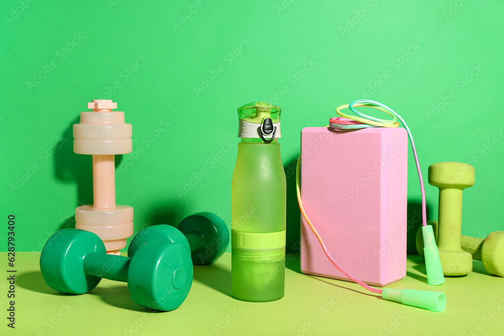 Set of sports equipment with bottle of water on green background