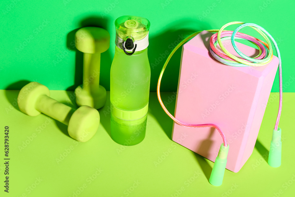 Set of sports equipment with bottle of water on green background