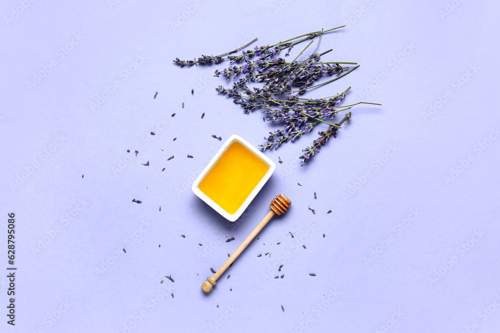 Bowl of sweet lavender honey, dipper and flowers on blue background