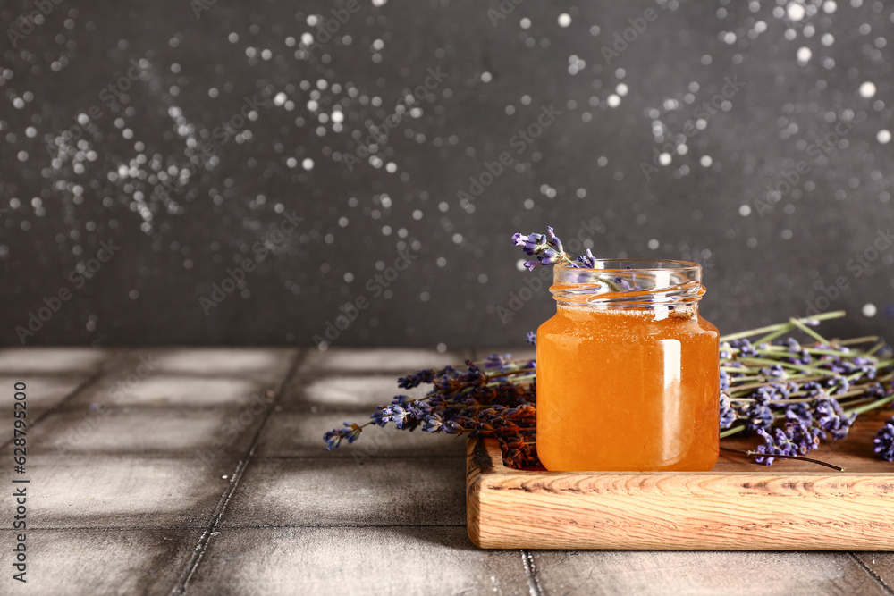 Wooden board with jar of sweet lavender honey and flowers on grey tile table