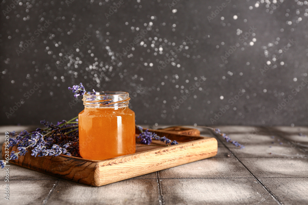 Wooden board with jar of sweet lavender honey and flowers on grey tile table