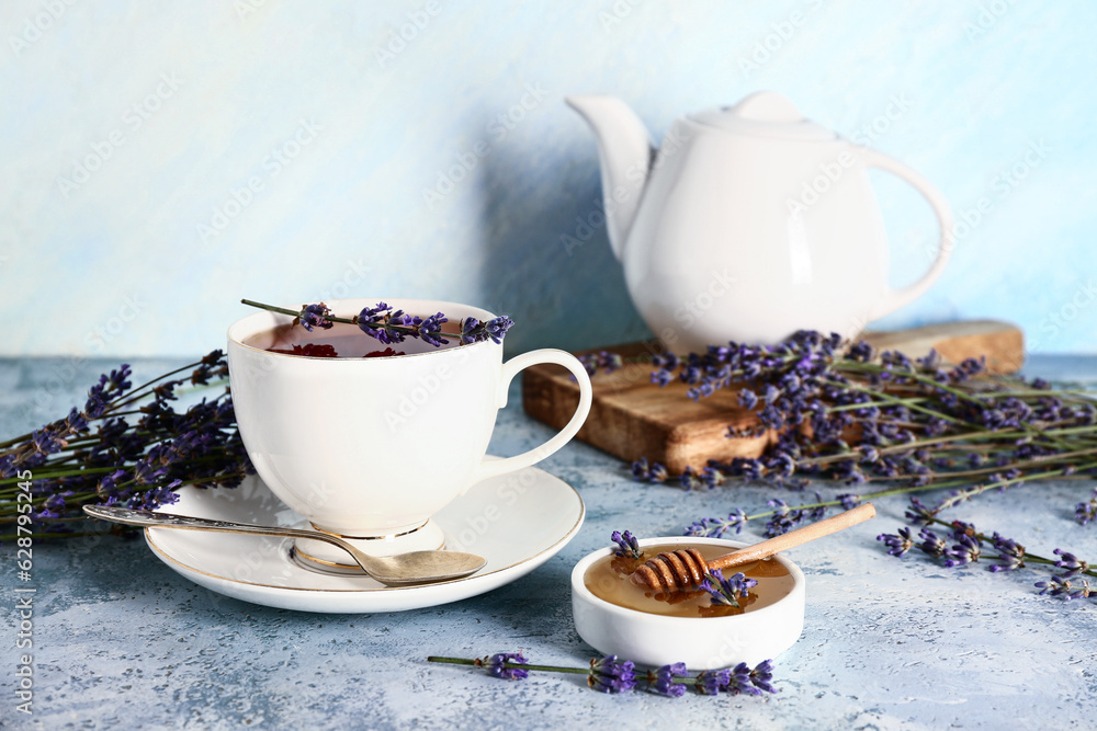 Bowl with sweet lavender honey and cup of tea on blue table