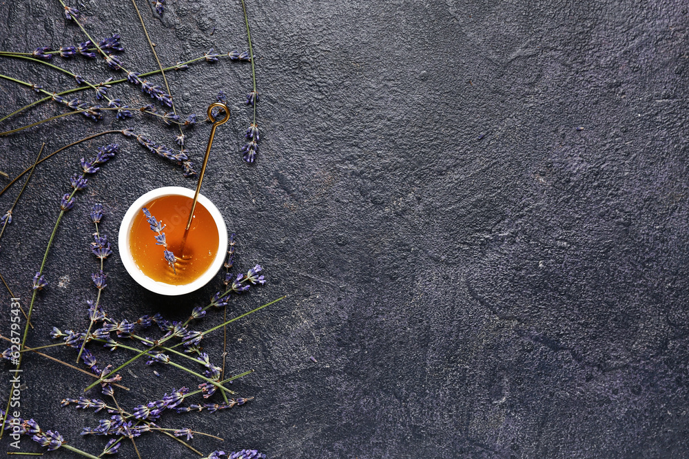 Bowl of sweet lavender honey, dipper and flowers on dark background