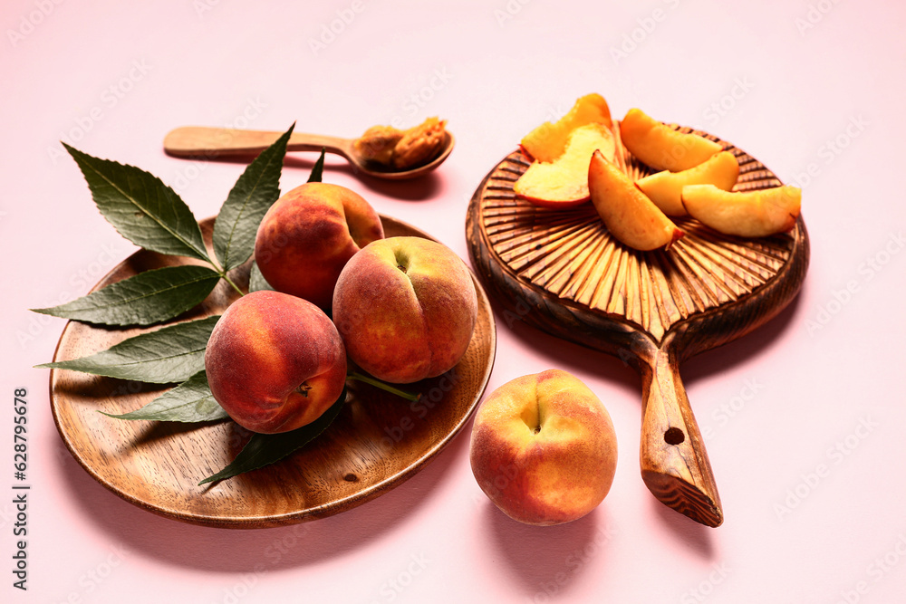 Plate of sweet peaches and wooden board with pieces on pink background