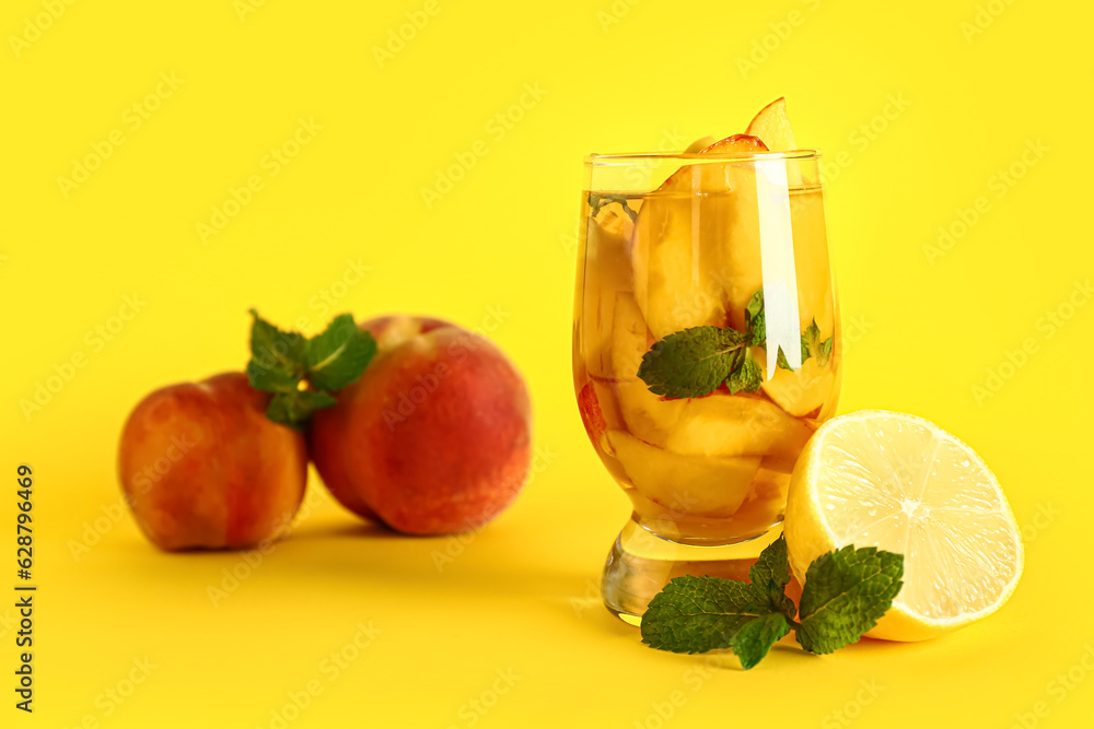 Glass of fresh peach lemonade with mint on yellow background