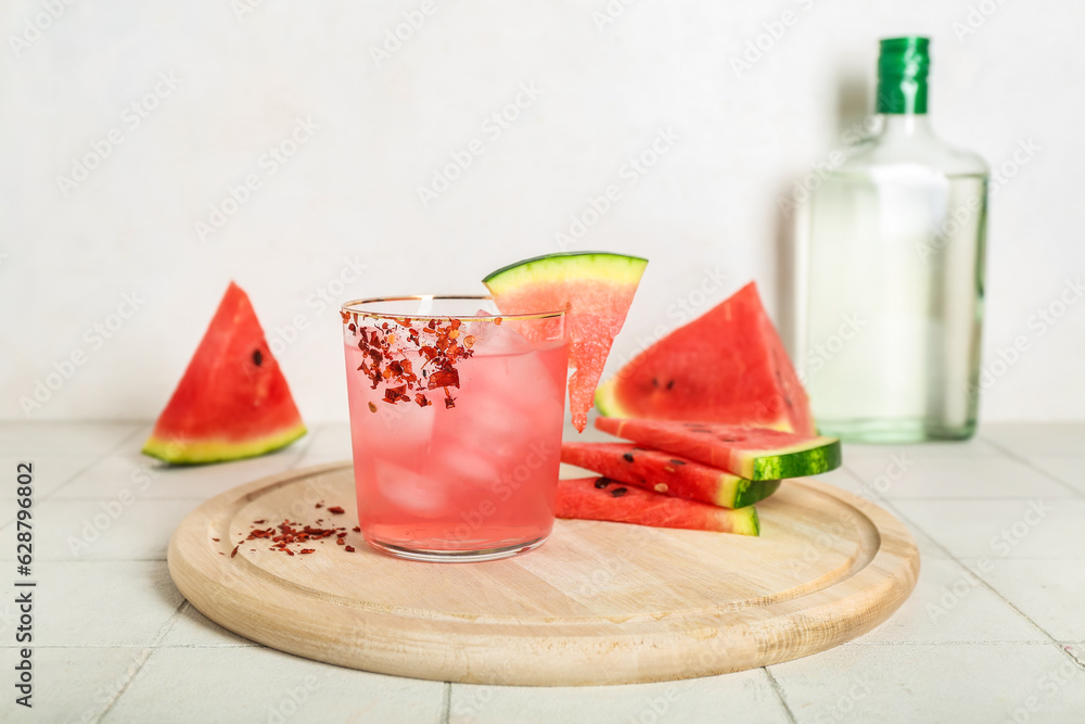 Board with glass of tasty watermelon cocktail and bottle on white tile background