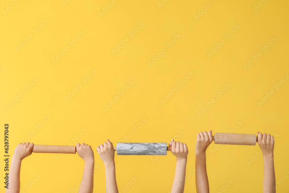 Female hands with rolling pins on yellow background