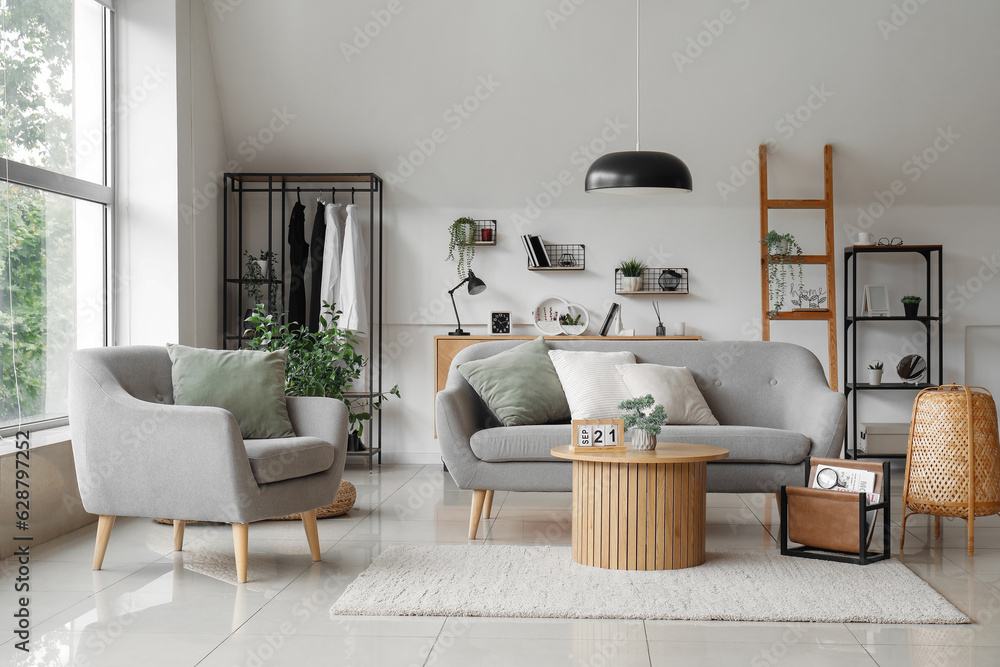 Interior of light living room with grey sofa, armchair and wooden coffee table