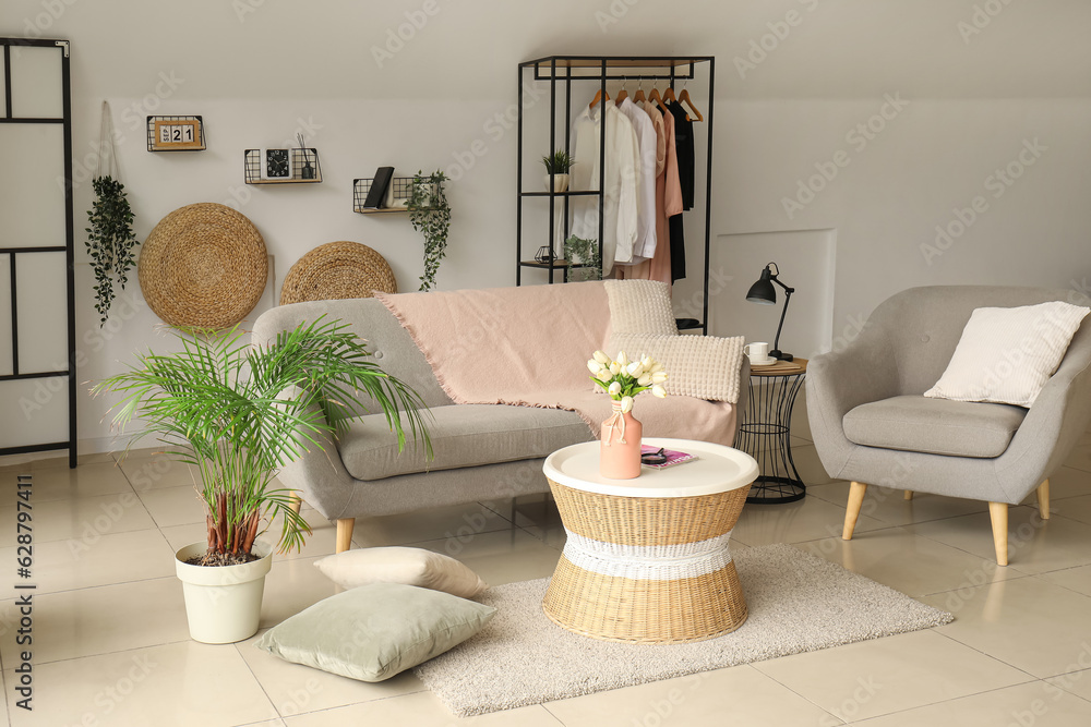 Interior of light living room with comfortable grey sofa, armchair and coffee table