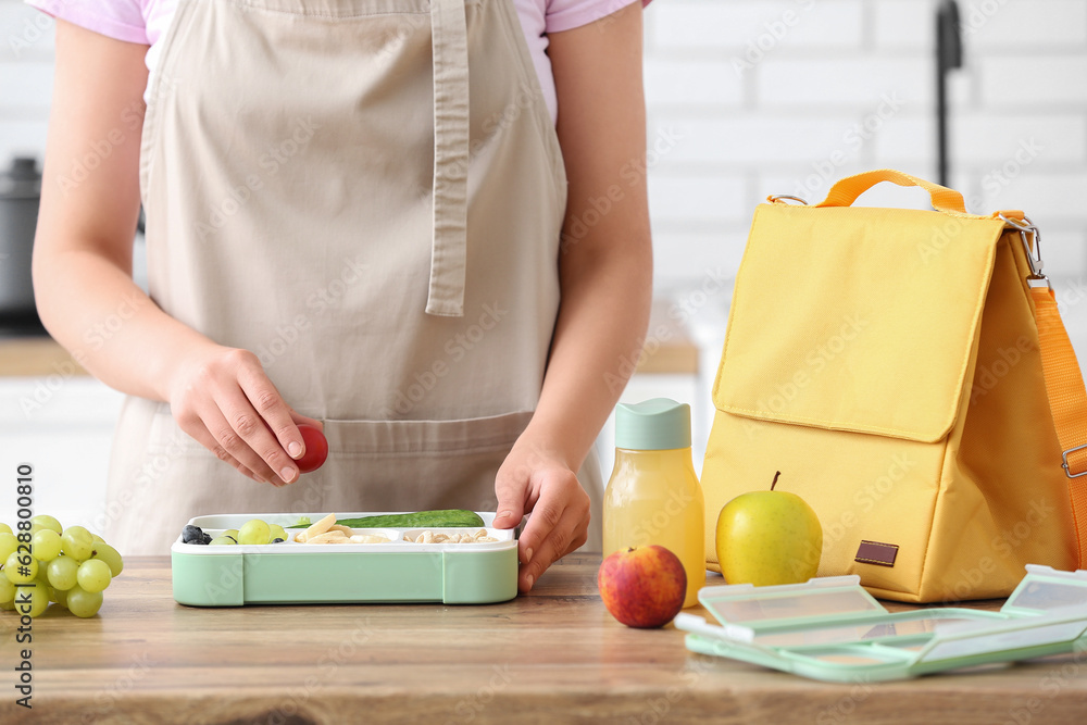 Woman packing fresh meal into lunch box in kitchen