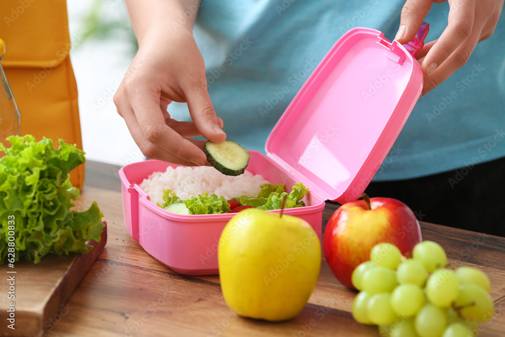 Woman packing fresh meal into lunch box in kitchen