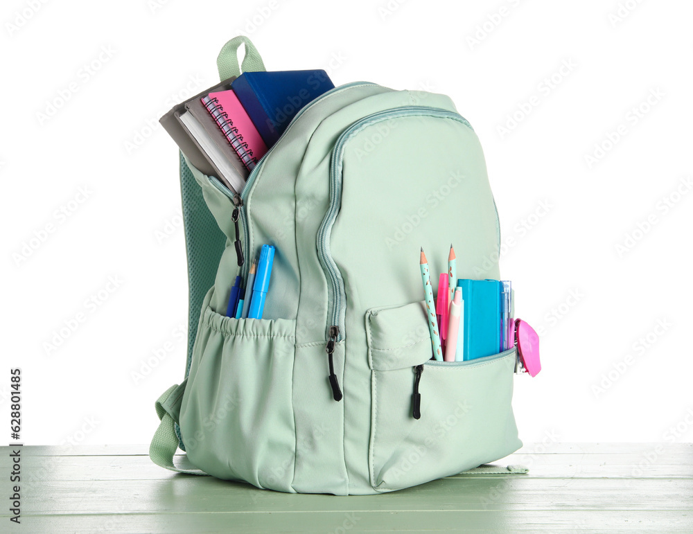 Green school backpack with notebooks, pencils and pens on wooden table near white background