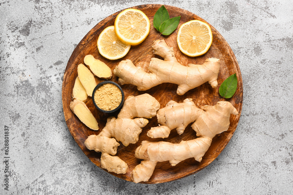 Wooden board with fresh ginger roots, sliced lemon and bowl of dried powder on grey background