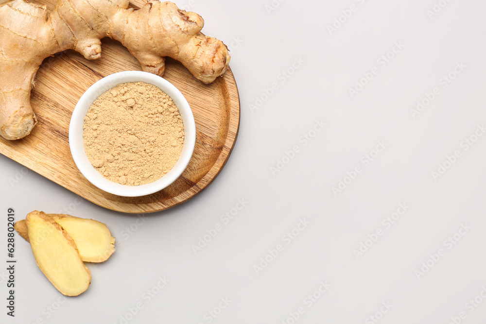 Wooden board with fresh ginger root and bowl of dried powder on grey background