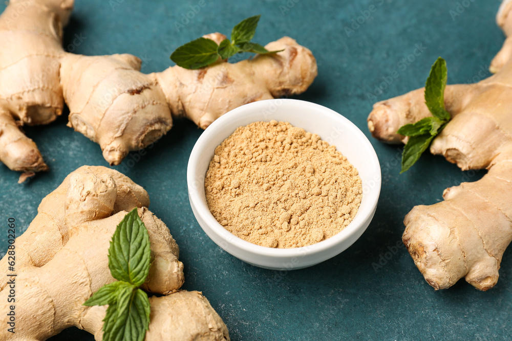 Fresh ginger roots and bowl with dried powder on blue background