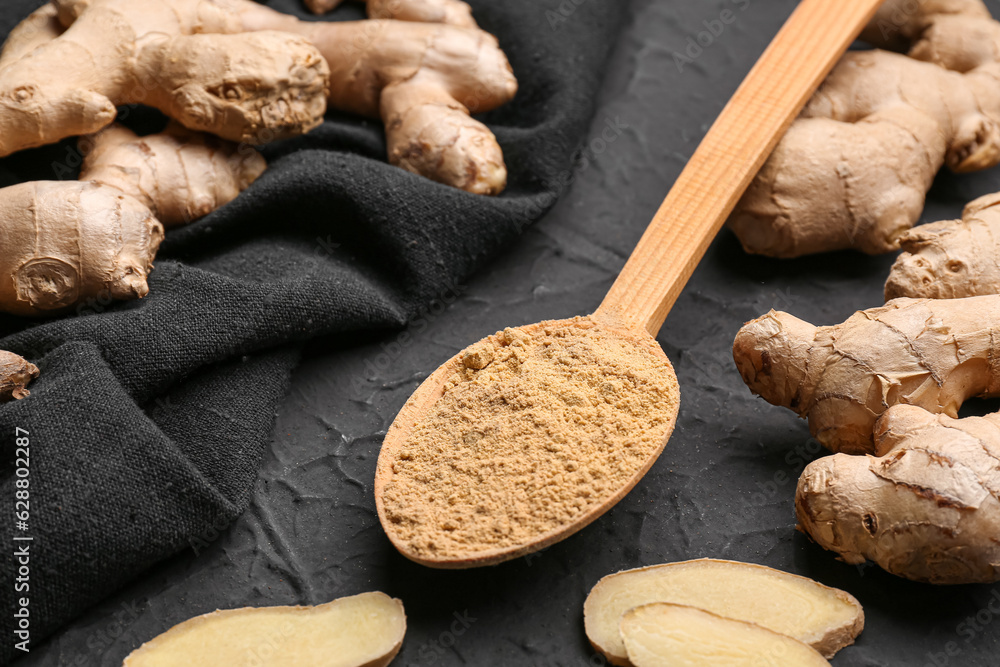 Fresh ginger roots and wooden spoon with dried powder on black background