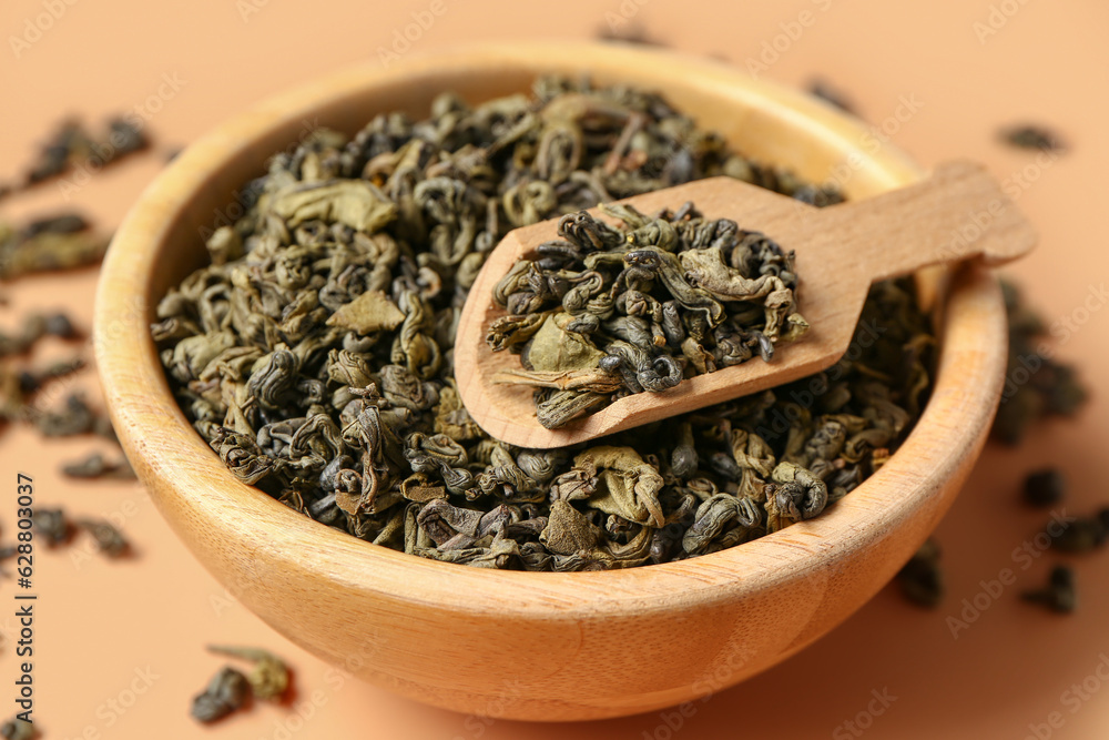 Wooden bowl and scoop with dry tea leaves on orange background