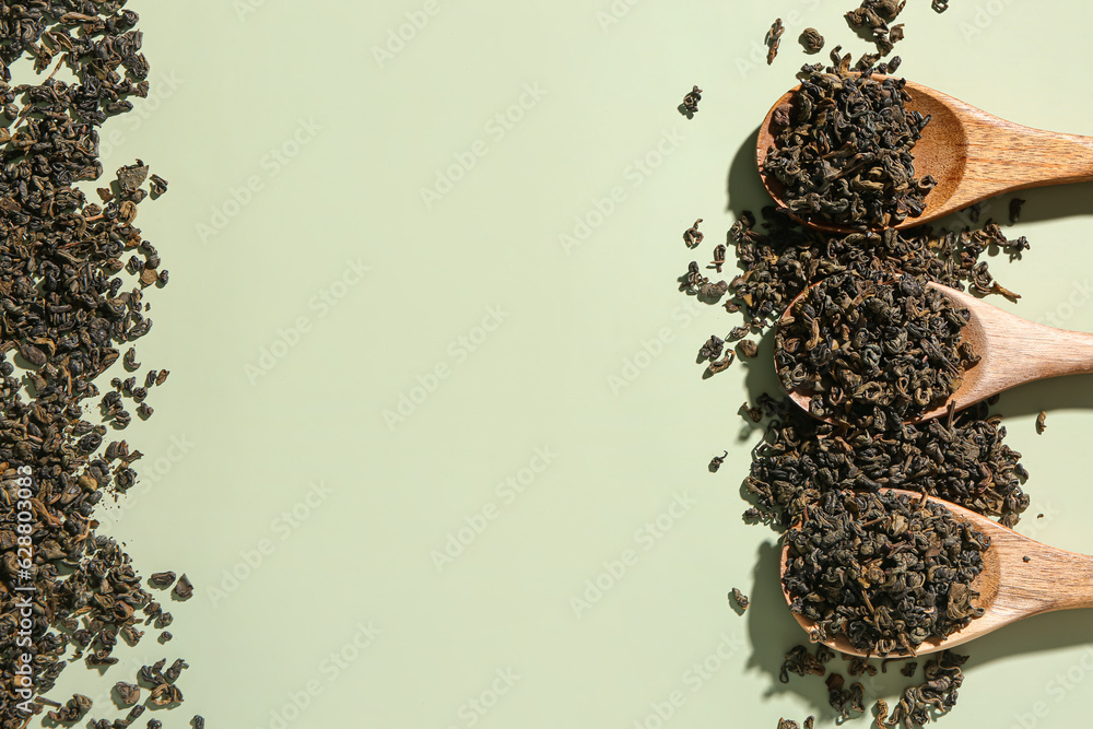 Wooden spoons with dry tea leaves on green background