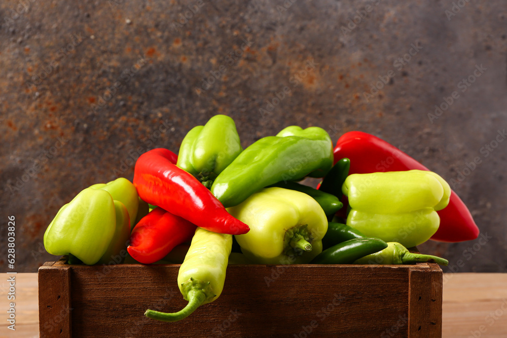 Box with different fresh peppers on wooden table