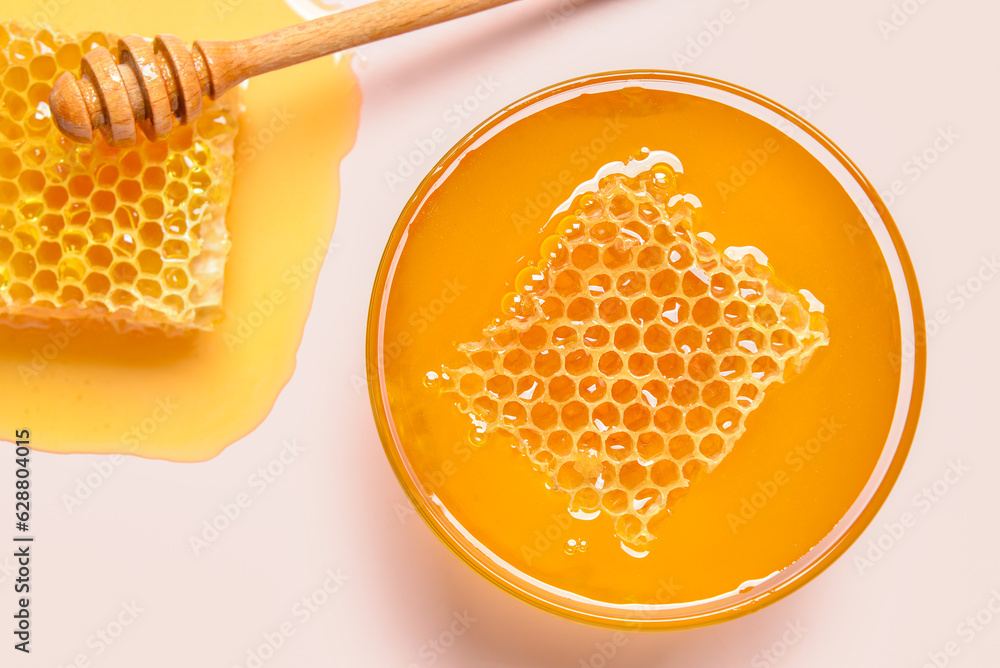 Glass bowl with sweet honey and combs on pink background