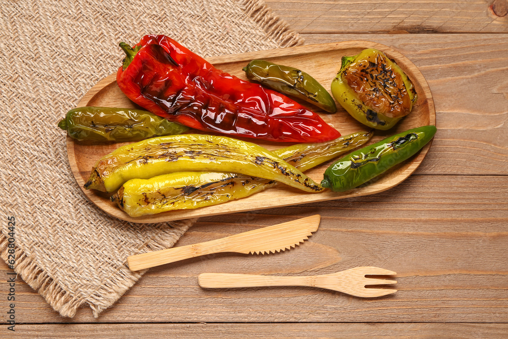 Board with different grilled peppers on wooden background