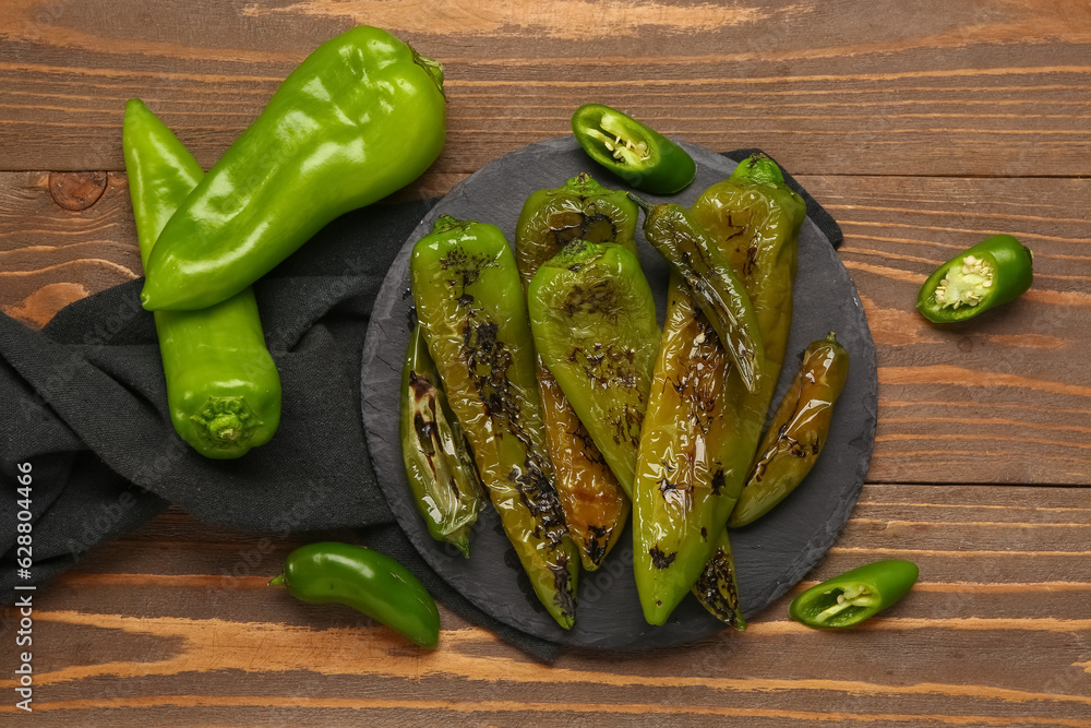 Slate board with grilled chili peppers on wooden background