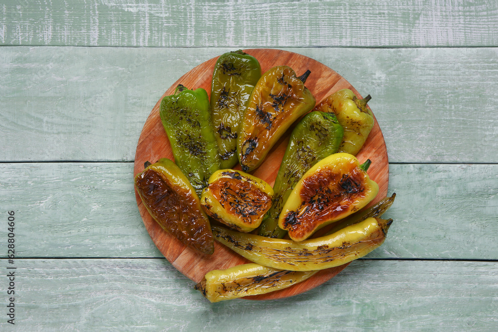 Board with different grilled peppers on green wooden background