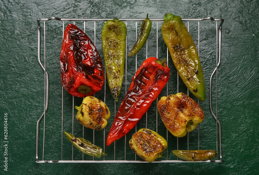 Cooling rack with different grilled peppers on green background