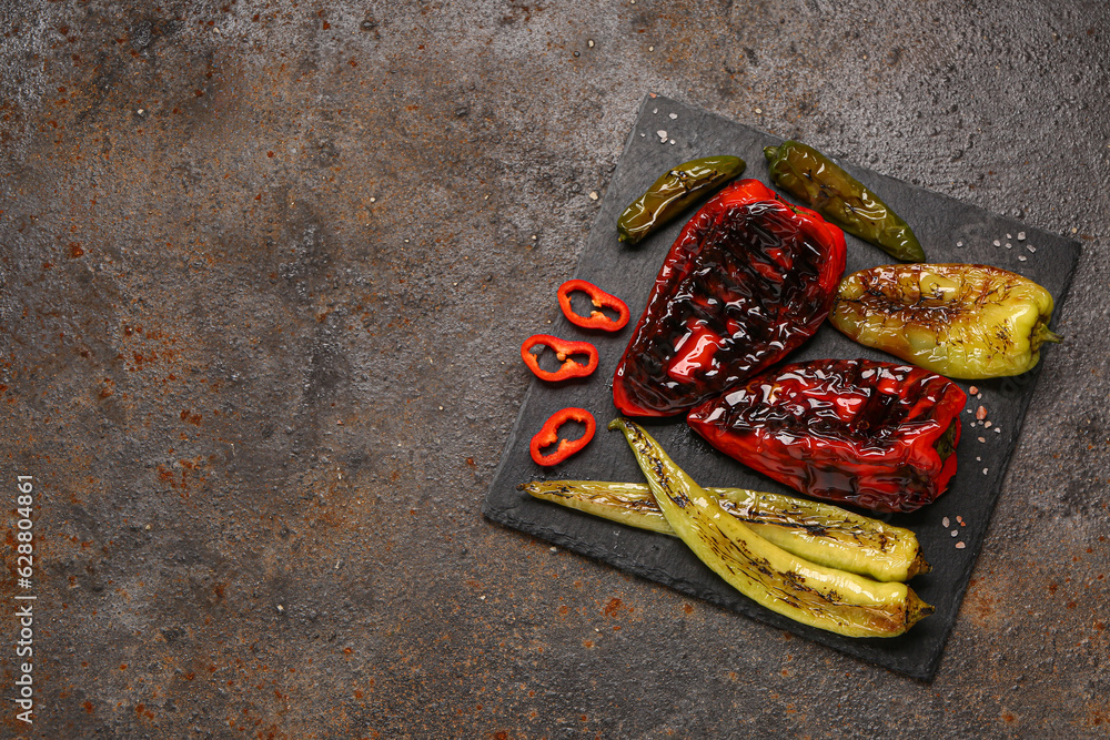 Board with different grilled peppers on dark background