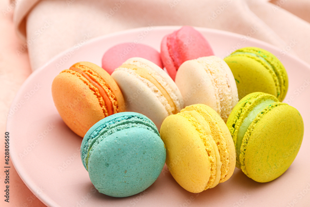 Plate with sweet macaroons on pink background