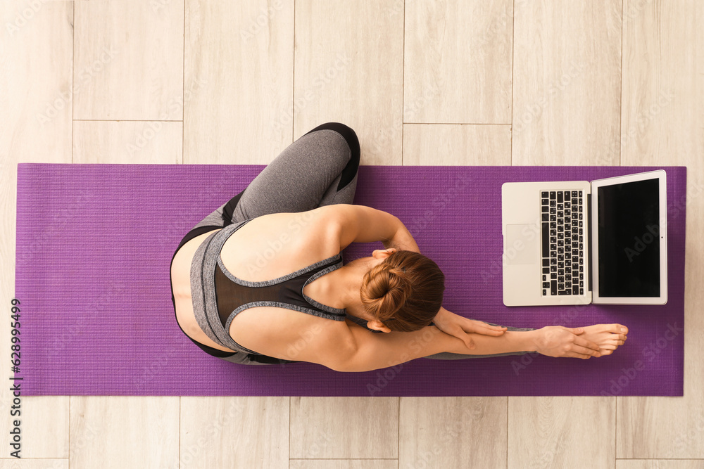 Sporty young woman with laptop doing yoga in gym, top view