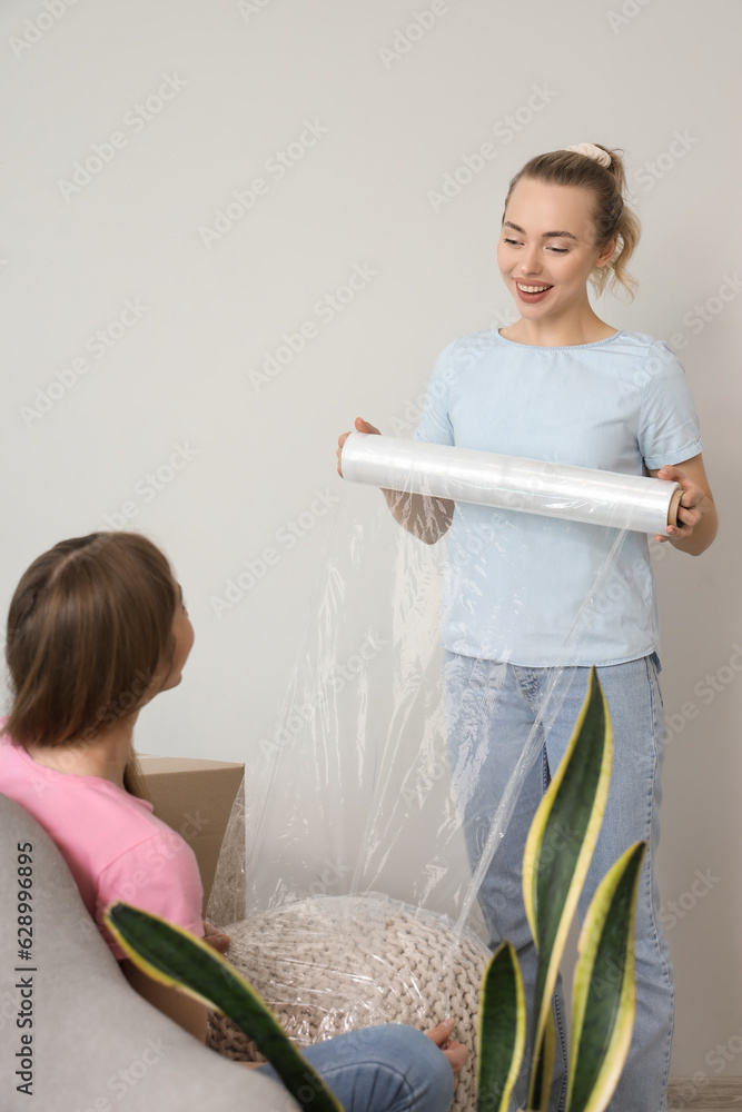 Young women wrapping pouf with stretch film at home