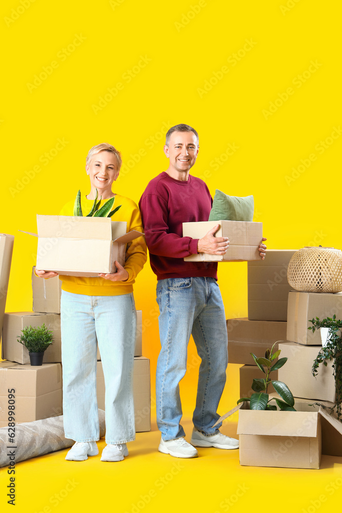 Mature couple with moving boxes on yellow background