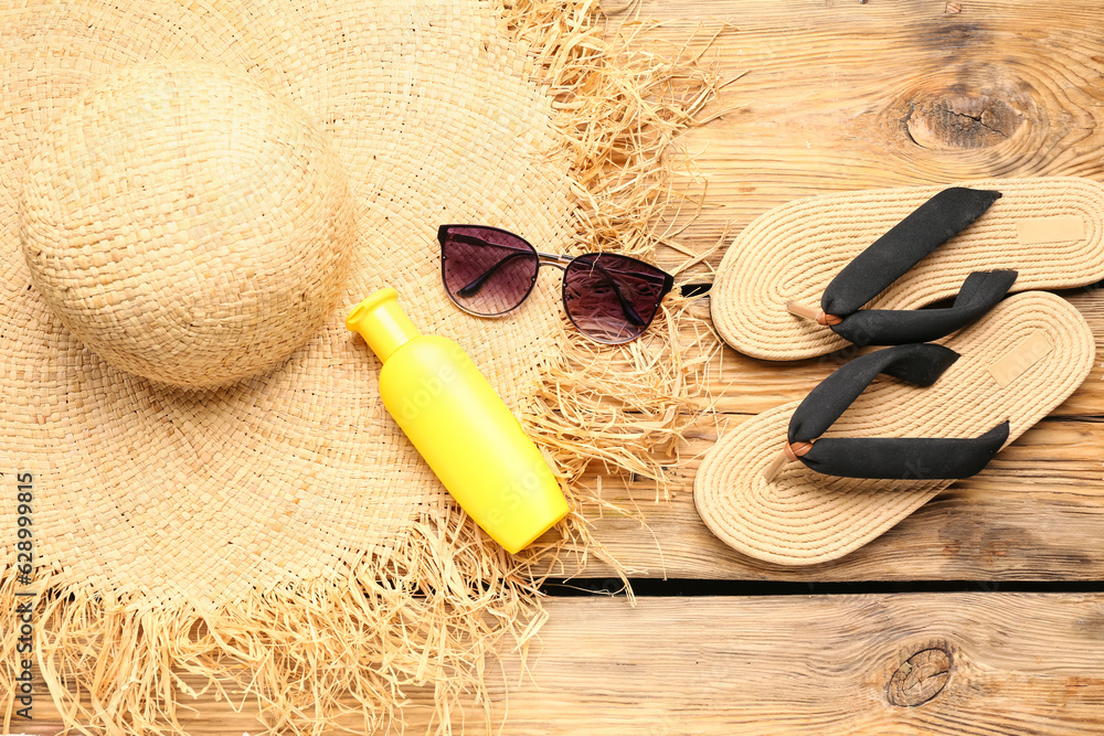 Sunglasses with flip flops, wicker hat and bottle of sunscreen cream on wooden background